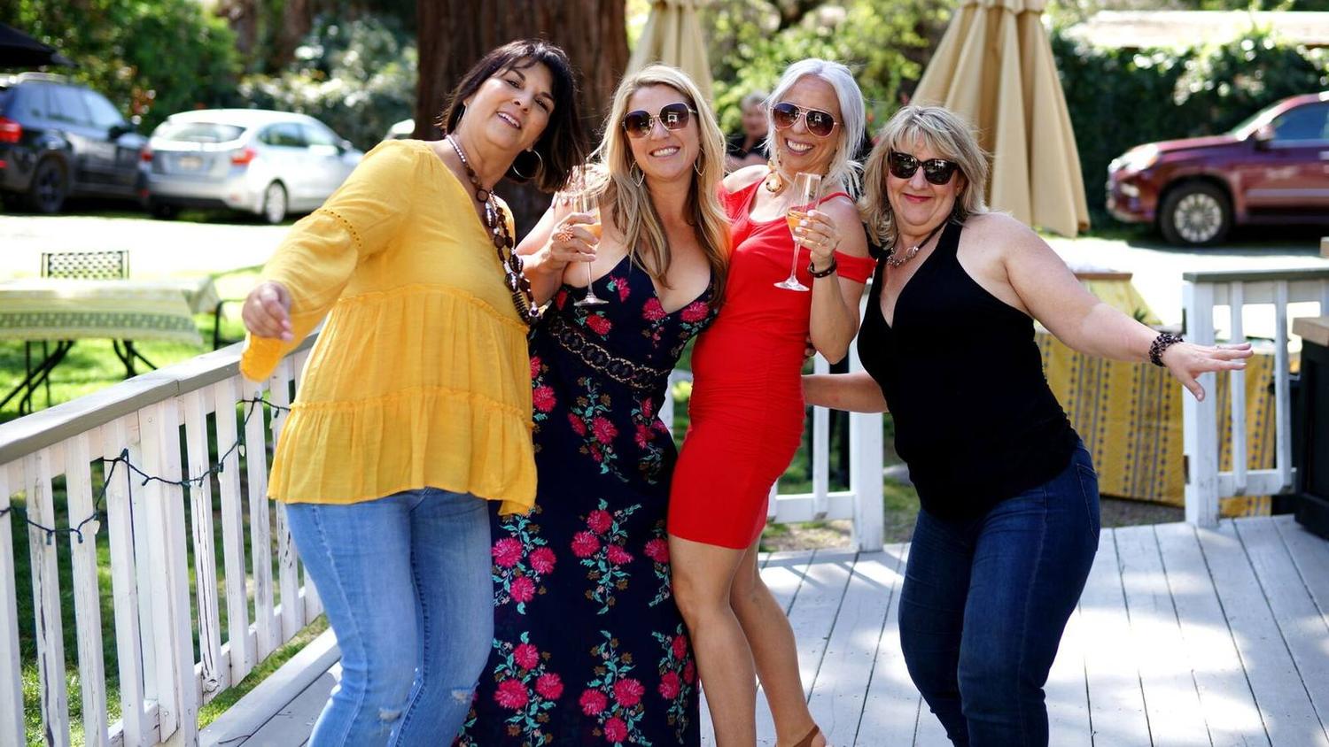 Four friends laughing on a porch with glasses in hand