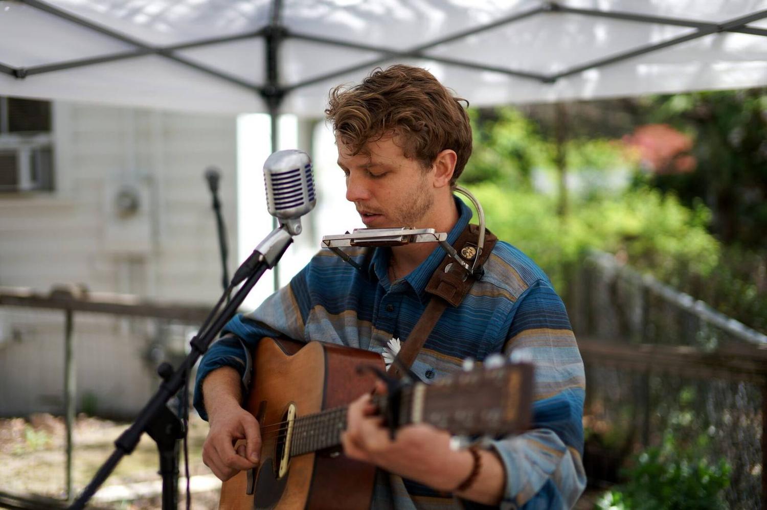 A guitarist singing into a vintage microphone outdoors
